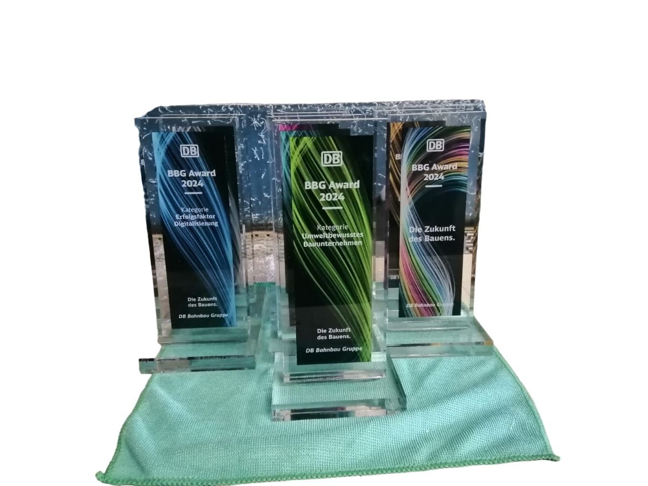 Three BBG Award 2024 trophies with colorful designs displayed on a light green cloth.